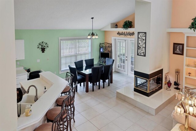 tiled dining space featuring a notable chandelier, french doors, and high vaulted ceiling