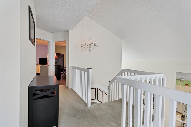 hall with an inviting chandelier, a textured ceiling, lofted ceiling, and carpet flooring