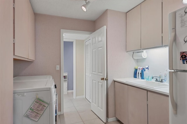 laundry area with light tile patterned floors, a textured ceiling, washing machine and clothes dryer, cabinets, and sink