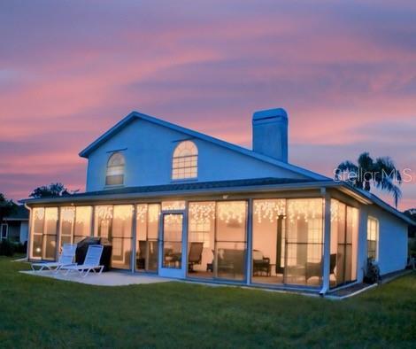 back house at dusk featuring a sunroom and a lawn