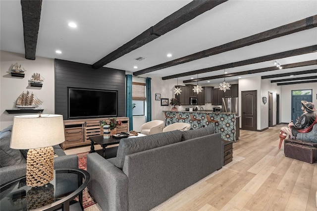 living room featuring beamed ceiling, light hardwood / wood-style floors, a healthy amount of sunlight, and a chandelier