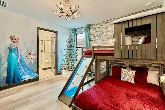 bedroom featuring a notable chandelier, ensuite bath, a textured ceiling, and light wood-type flooring