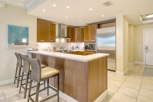 915 Seaside Drive 607, Weeks 14-15, Sarasota, FL 34242 - kitchen with wall chimney range hood, built in appliances, a peninsula, brown cabinets, and ornamental molding