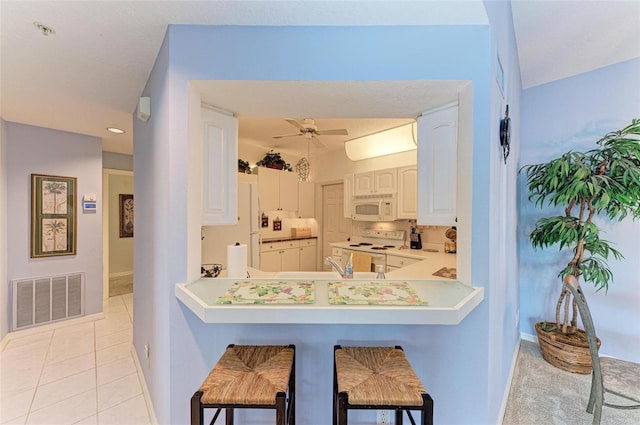 kitchen featuring light tile patterned floors, white appliances, a kitchen breakfast bar, white cabinets, and kitchen peninsula