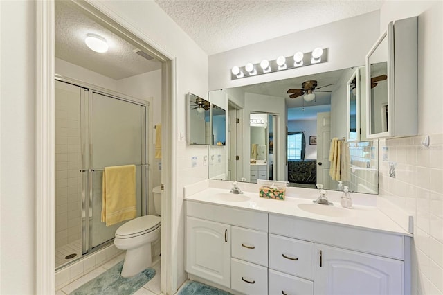 bathroom featuring a shower with shower door, vanity, ceiling fan, toilet, and a textured ceiling