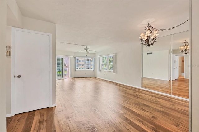 empty room with ceiling fan with notable chandelier and hardwood / wood-style floors