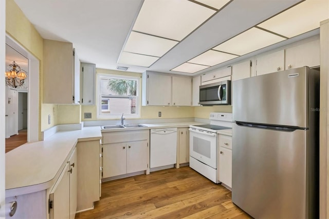 kitchen with sink, appliances with stainless steel finishes, kitchen peninsula, and light wood-type flooring