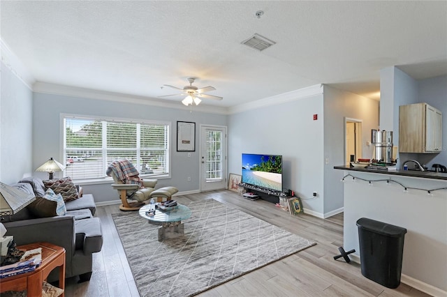 living room with ceiling fan, crown molding, a textured ceiling, and light wood-type flooring