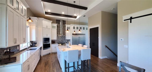 kitchen featuring a kitchen island, white cabinets, built in appliances, and wall chimney range hood