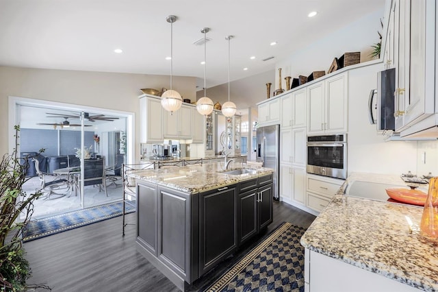 kitchen with dark wood-type flooring, pendant lighting, stainless steel appliances, a kitchen island with sink, and white cabinets