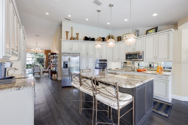 kitchen featuring appliances with stainless steel finishes, sink, white cabinets, hanging light fixtures, and a center island with sink