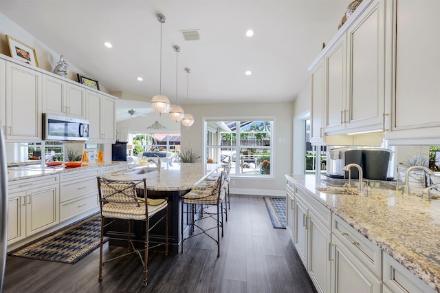 kitchen featuring pendant lighting, lofted ceiling, a kitchen bar, and light stone countertops