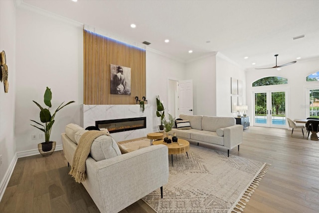 living room featuring french doors, ornamental molding, ceiling fan, light hardwood / wood-style flooring, and a premium fireplace