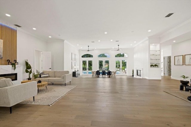 living room with a high end fireplace, french doors, crown molding, light hardwood / wood-style flooring, and ceiling fan