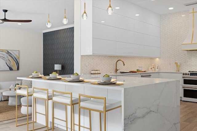 kitchen featuring pendant lighting, stove, white cabinets, sink, and light stone counters