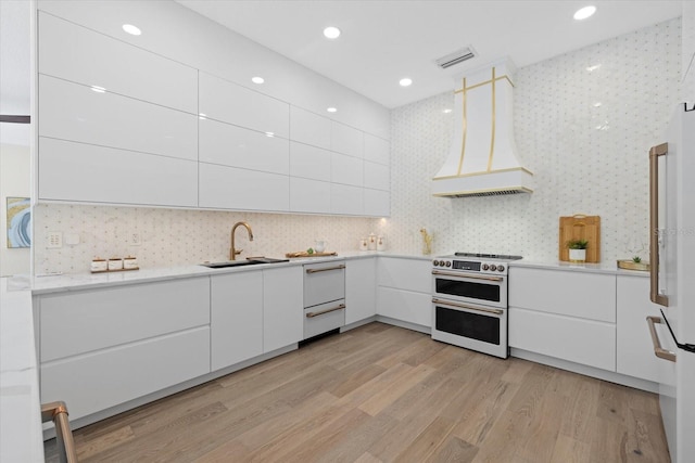 kitchen featuring premium range hood, sink, white cabinets, and range with two ovens