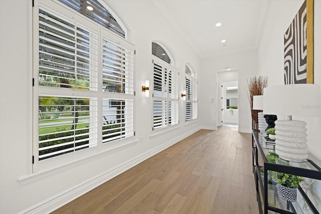 hallway with wood finished floors, recessed lighting, arched walkways, crown molding, and baseboards