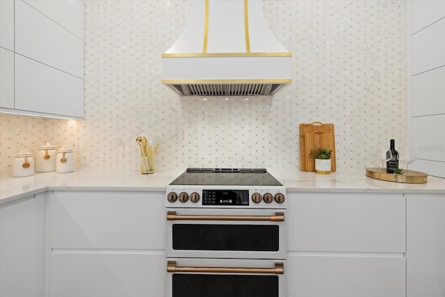 kitchen featuring light stone countertops, premium range hood, white range with electric cooktop, white cabinetry, and backsplash