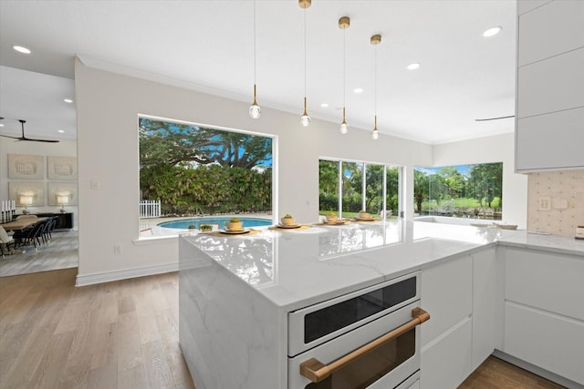 kitchen with white cabinets, decorative light fixtures, light stone countertops, and light wood-type flooring