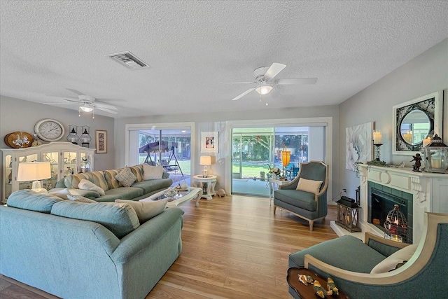 living room featuring a tiled fireplace, a textured ceiling, light hardwood / wood-style flooring, and ceiling fan