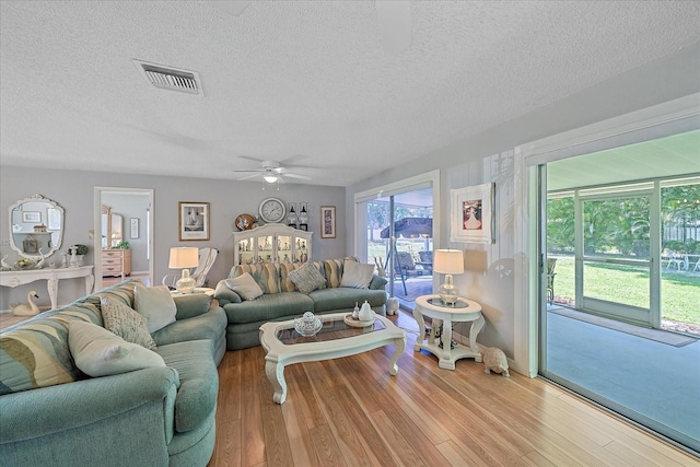 living room with ceiling fan, light hardwood / wood-style floors, and a textured ceiling