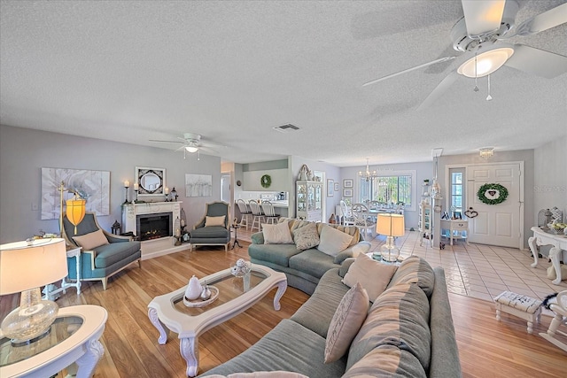 living room with ceiling fan with notable chandelier, a textured ceiling, and light wood-type flooring