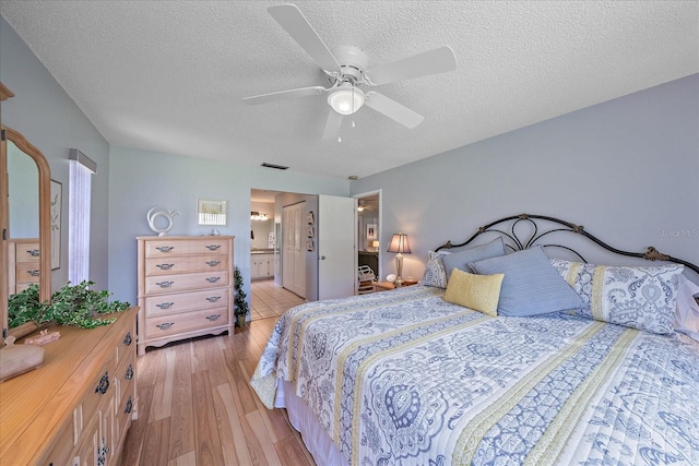 bedroom featuring ceiling fan, ensuite bath, light hardwood / wood-style floors, and a textured ceiling