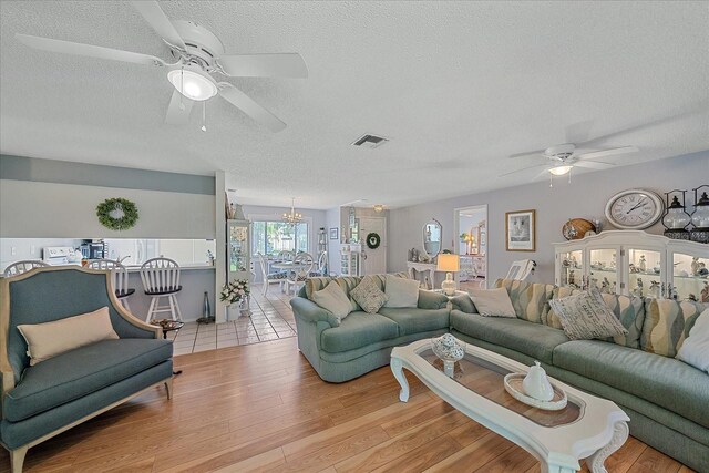 living room with ceiling fan with notable chandelier, a textured ceiling, and light wood-type flooring