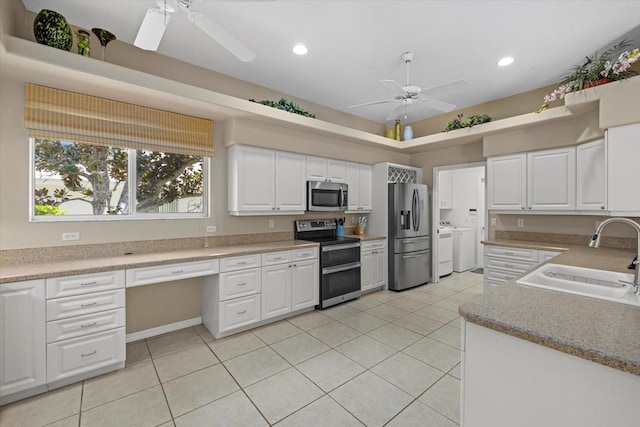 kitchen featuring appliances with stainless steel finishes, built in desk, washing machine and dryer, white cabinetry, and sink