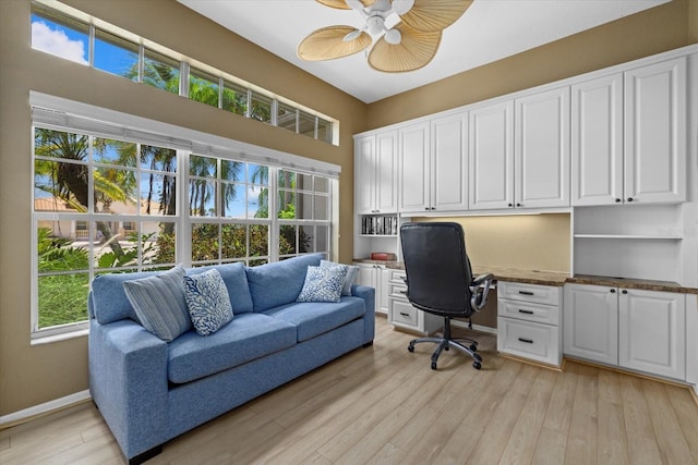 office space featuring built in study area, light wood-style flooring, baseboards, and ceiling fan