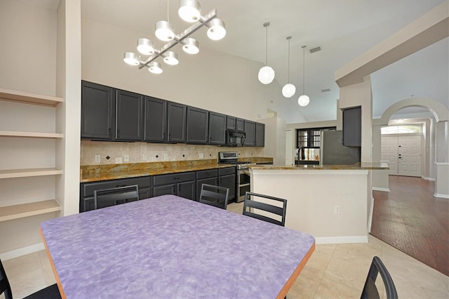 kitchen with appliances with stainless steel finishes, light tile patterned floors, pendant lighting, built in features, and a high ceiling