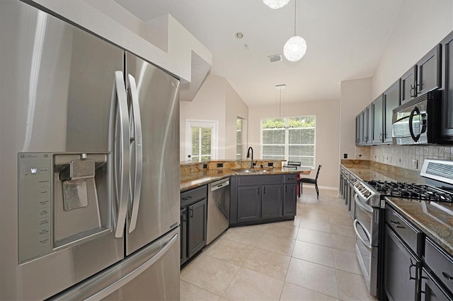 kitchen featuring appliances with stainless steel finishes, vaulted ceiling, sink, decorative light fixtures, and dark stone countertops