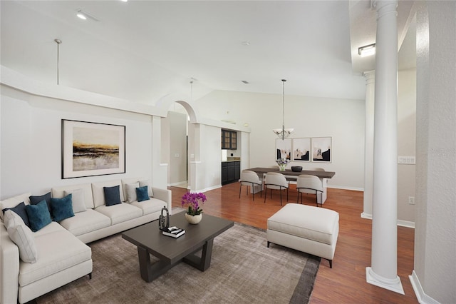 living room with ornate columns, a notable chandelier, lofted ceiling, and hardwood / wood-style flooring