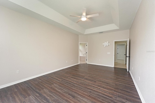 empty room with a raised ceiling, ceiling fan, and dark wood-type flooring