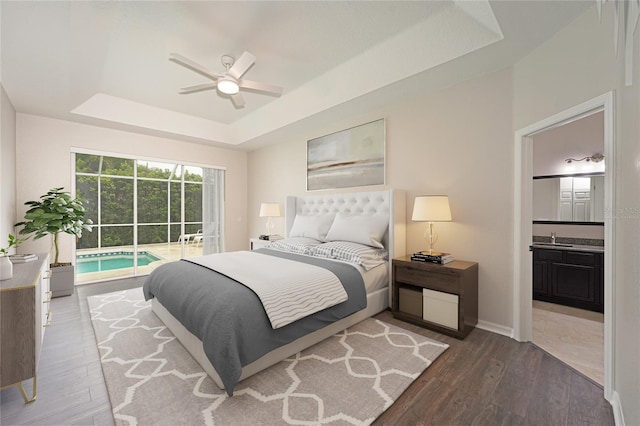 bedroom with ensuite bath, a tray ceiling, access to outside, ceiling fan, and hardwood / wood-style floors