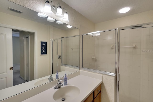 bathroom with a shower with door, vanity, and a textured ceiling