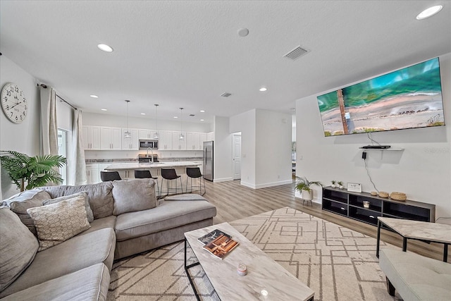 living area featuring light wood-type flooring, visible vents, a textured ceiling, and recessed lighting