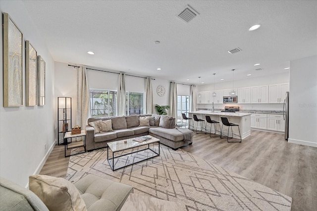 living area with visible vents, a textured ceiling, and light wood finished floors