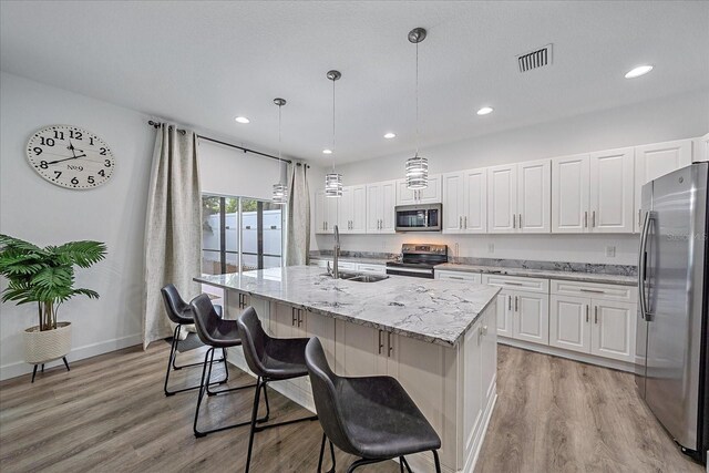 kitchen featuring white cabinetry, light hardwood / wood-style flooring, stainless steel appliances, hanging light fixtures, and sink