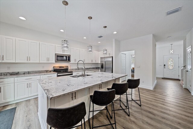 kitchen with light wood-type flooring, hanging light fixtures, sink, appliances with stainless steel finishes, and a center island with sink