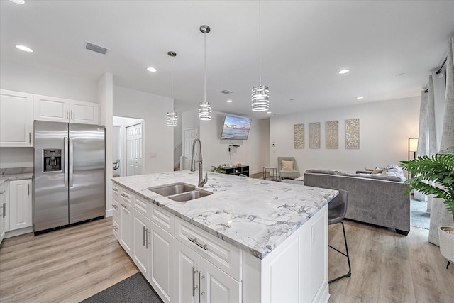 kitchen with white cabinetry, stainless steel fridge with ice dispenser, an island with sink, sink, and light hardwood / wood-style flooring