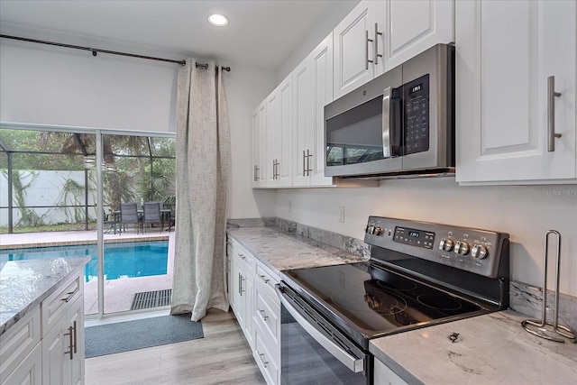 kitchen featuring white cabinetry, stainless steel appliances, light stone countertops, and light wood-type flooring