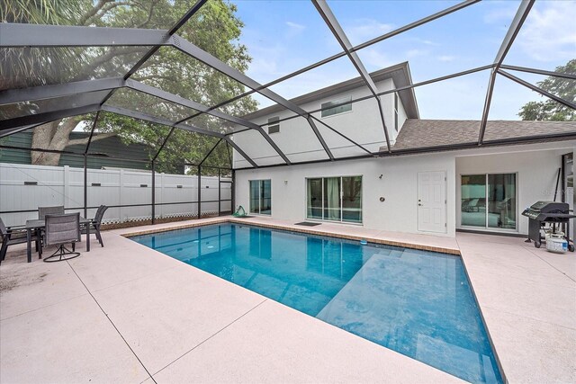 view of pool with grilling area, a patio area, and glass enclosure