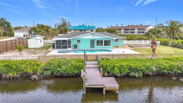 rear view of house with a sunroom, a storage shed, a patio area, a fenced in pool, and a water view