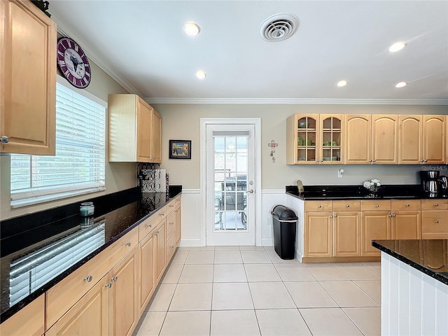 kitchen featuring light brown cabinetry, crown molding, and dark stone countertops