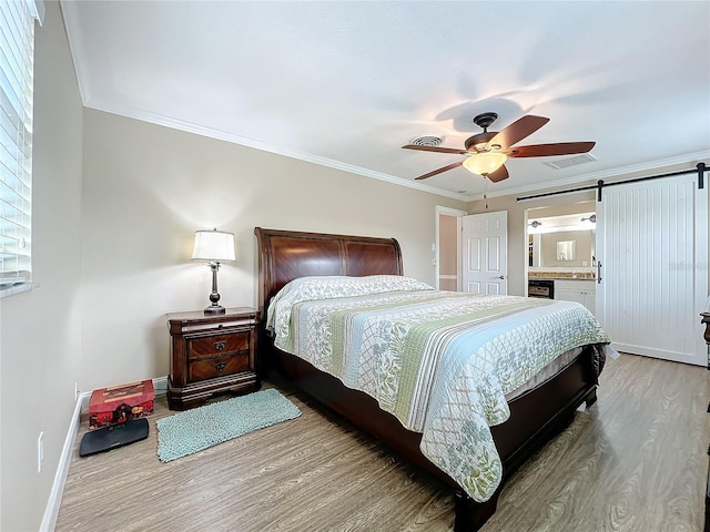 bedroom with ornamental molding, light wood-type flooring, ceiling fan, ensuite bathroom, and a barn door