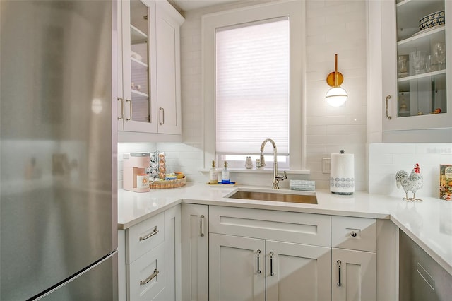 kitchen featuring tasteful backsplash, stainless steel fridge, sink, and white cabinets