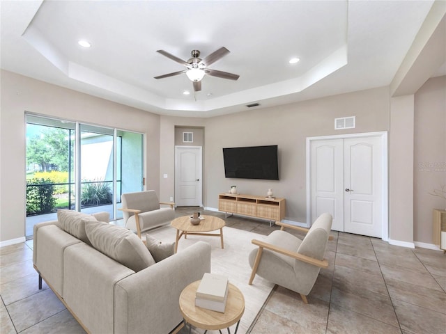 living room featuring light tile patterned flooring, a ceiling fan, visible vents, baseboards, and a tray ceiling