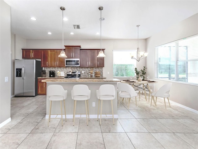 kitchen with pendant lighting, visible vents, appliances with stainless steel finishes, an island with sink, and a kitchen bar