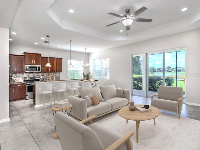 living area with a tray ceiling, recessed lighting, baseboards, and ceiling fan with notable chandelier